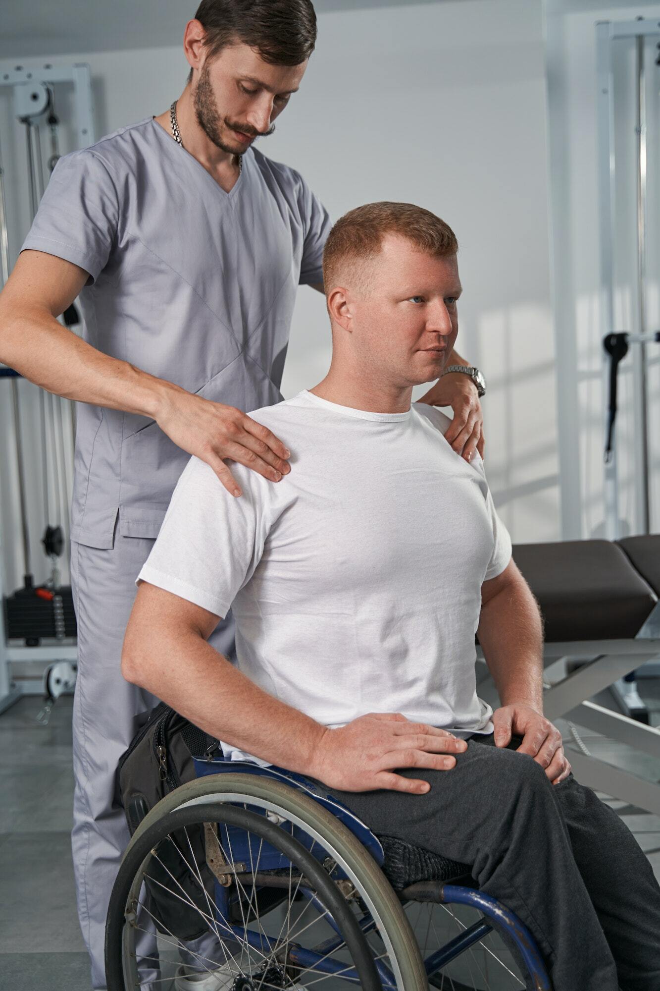 Caucasian doctor checks shoulders of patient with spinal cord injury